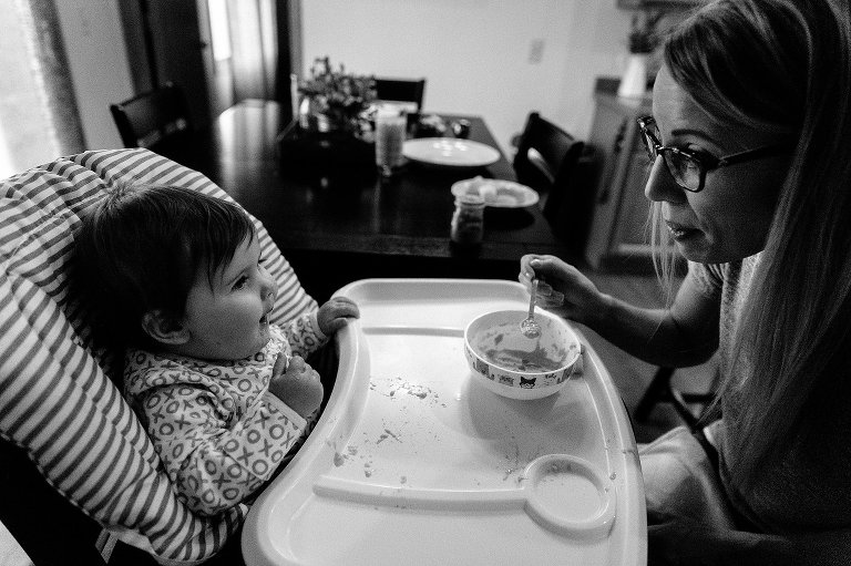 Mom holds spoon of baby cereal on a dark, early morning.