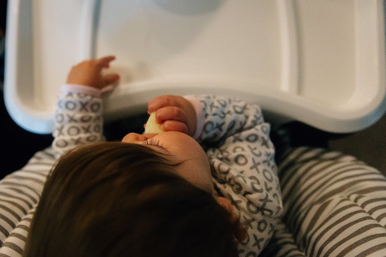 Top down view of baby's eyelashes. Baby sitting in high chair, feeding self a pear.