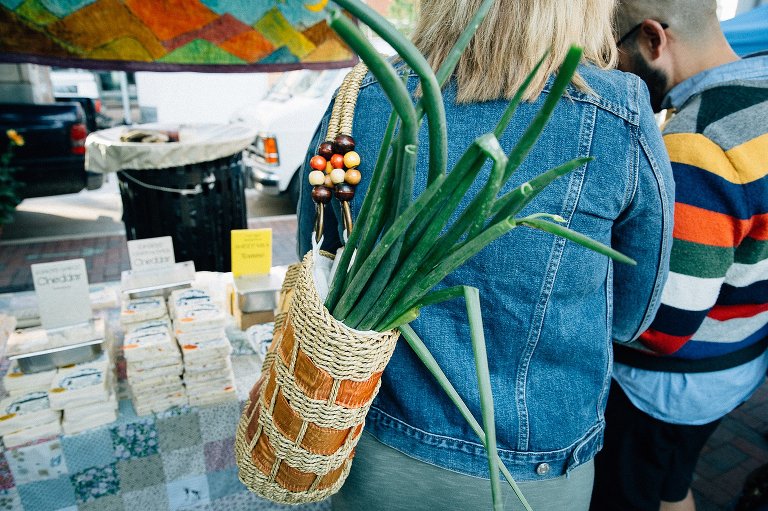Woman carries leeks at famers market in a straw bag 