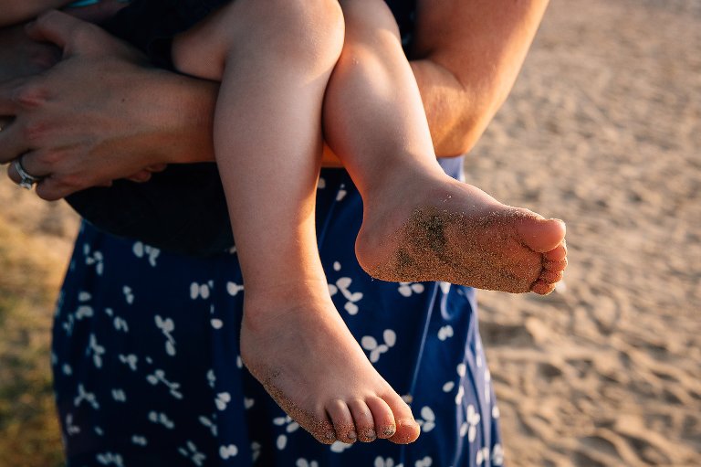 Mom holds young preschool son with sandy feet. 