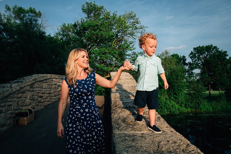 Mom holds young son's hand as he balanced on wide bridge edge.