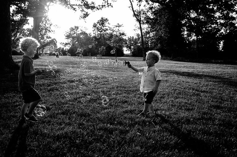 Black and white photo of two young brothers playing bubbles in the park.