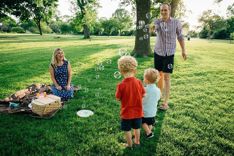 Dad plays bubbles with two young sons in the park. 
