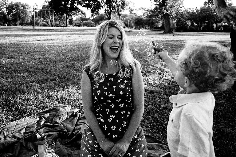 Black and white photo of young preschool boy blowing bubbles at his mother 
