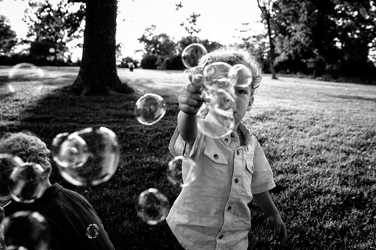 Black and white natural light photo of boy blowing bubbles at camera