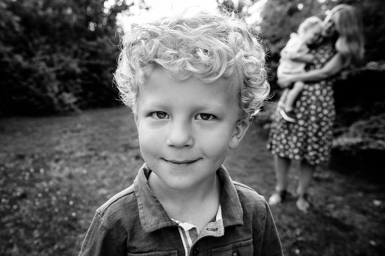 Black and white portrait of young boy. Mother holding younger son in background. 