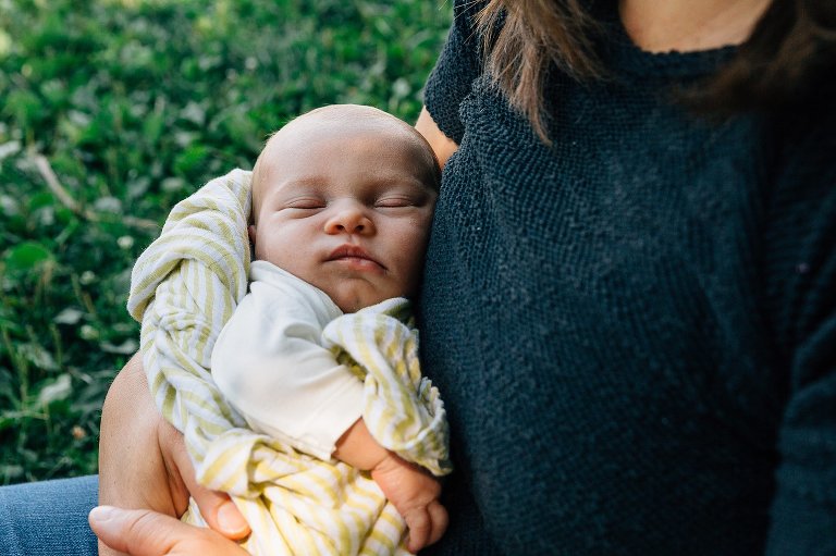 Newborn sleeps in mom's arms in the shade. 