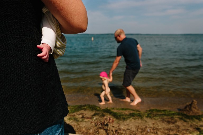 Focus on newborn's hands with Dad in background holding toddler's hand. 