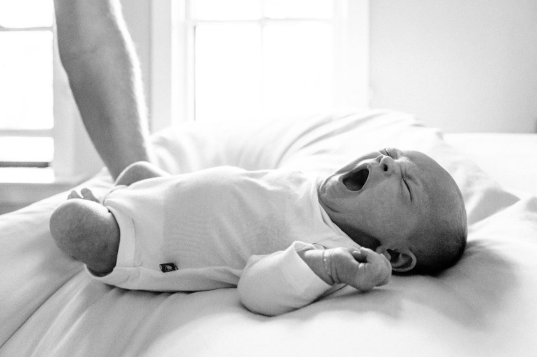 Newborn baby yawns on white bed. Black and white photo. 