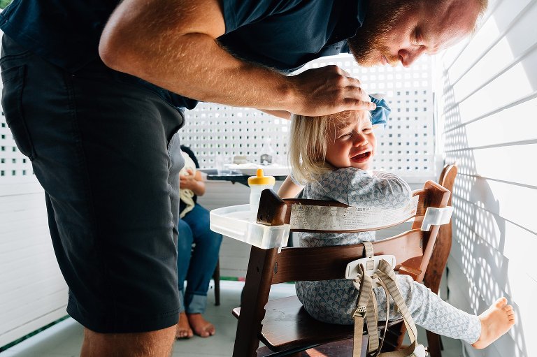 Dad wipes toddler daughter's face while she cries. 