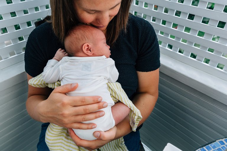 Mom holds newborn baby on porch. 