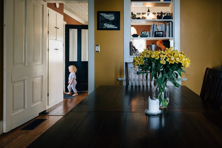 Summer flowers sit in formal dining room, while toddler girl walks through scene in the background. 