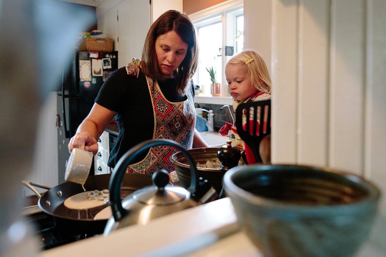 Mom pours blueberry pancake batter onto skillet. Daughter looks on. 