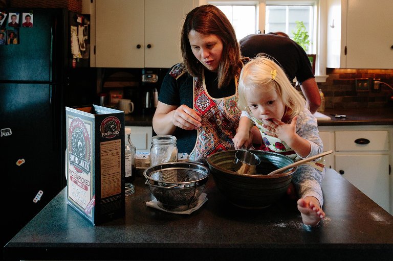 Mom and toddler daughter start to make pancakes. Toddler daughter licks batter. 