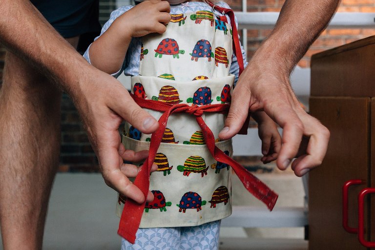 Dad ties apron around toddler daughter waist. 