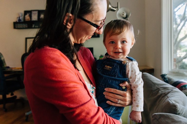 mothers hold a toddler girl in her arms, smiling, while in the living room of their home
