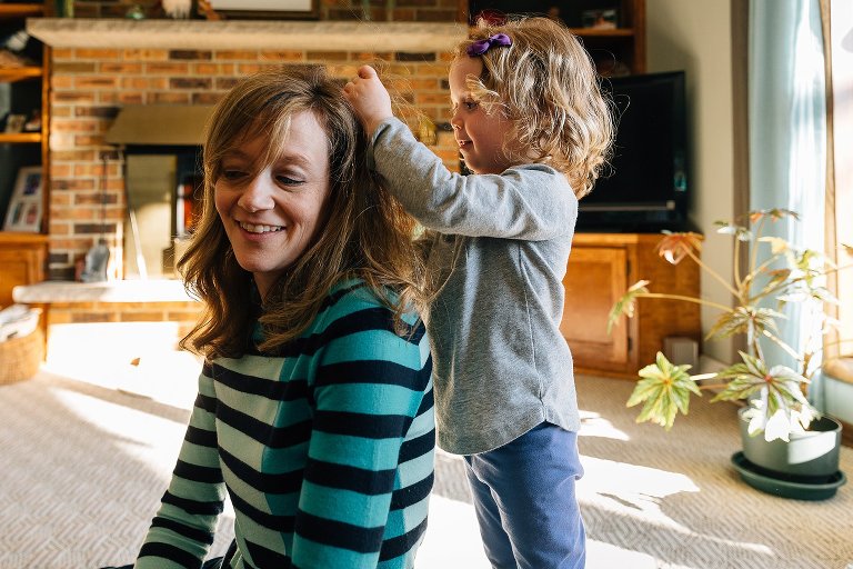 a child plays with her mothers hair in the living room. 