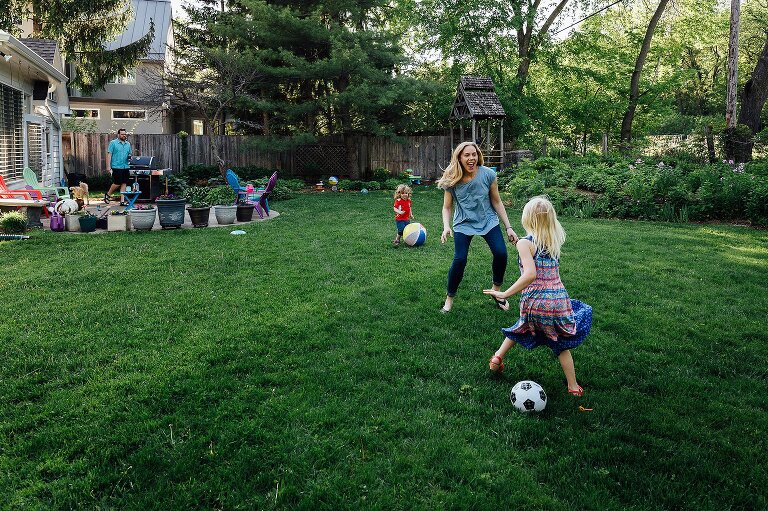 Mothers play soccer in the backyard with two young children