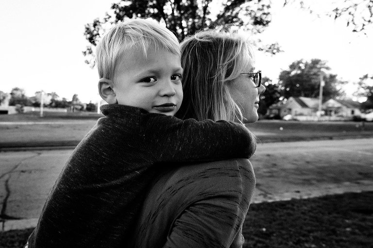 black. and white. Preschool boy smiles and makes eye contact with camera while getting a piggy back ride from his mother 