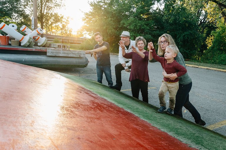 Parents and grandparents all show with their hands how a ski jumper would go up a ski jump if it were in the water. Ski jump is out of the lake, sitting in parking lot at the end of the season. 
