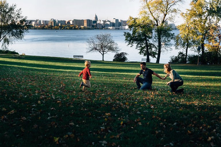 Boy runs to both parents down a big hill. City of Madison skyline in background 