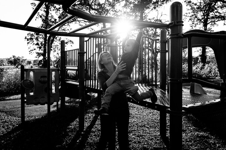Mom helps preschool boy across playground equipment 