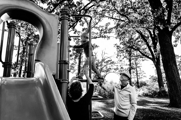 black and white. Grandparents are with grandson on playground equipment 