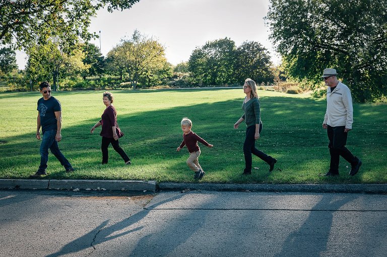 parents, grandparents, and small boy all walk in a line to the park.