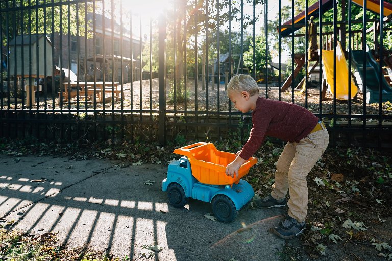 preschool boy plays with colorful dump truck outside a school playground 