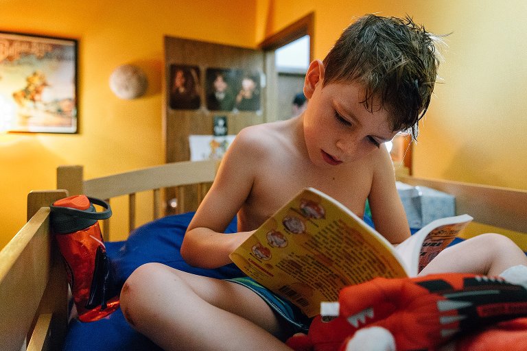 Young boy reads a chapter book in his top bunk 