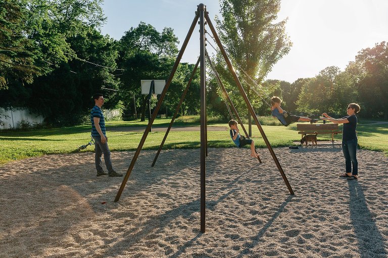 Parents on opposite of swing set with two boys on the swing .