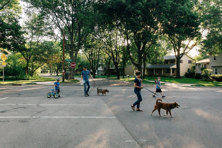 Family of four and two dogs all walk across the neighborhood street together. 