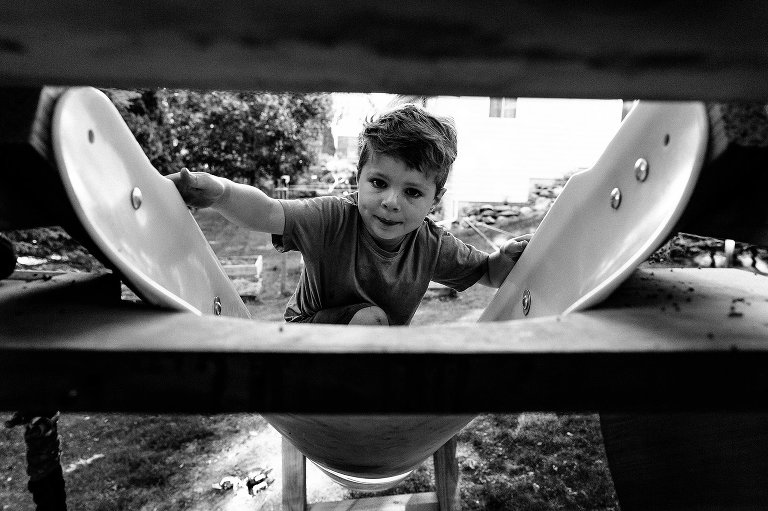 Boy climbs up a slide & makes eye contact with camera. Black and white. 