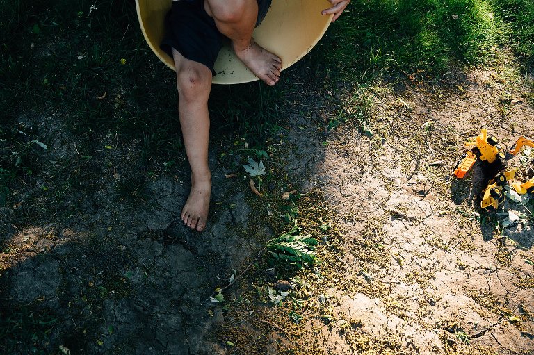 Top down view of boy coming off a yellow slide, barefoot. His knees and feet are dirty from playing outside all day. 