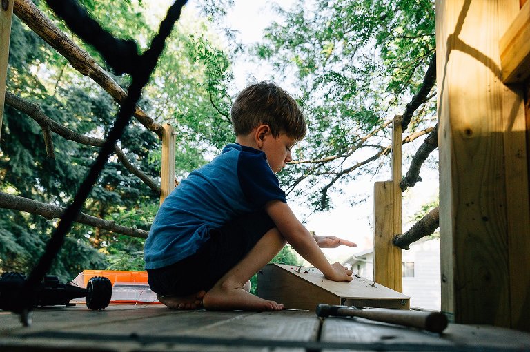Boy in treehouse works on electrical invention. Summertime.