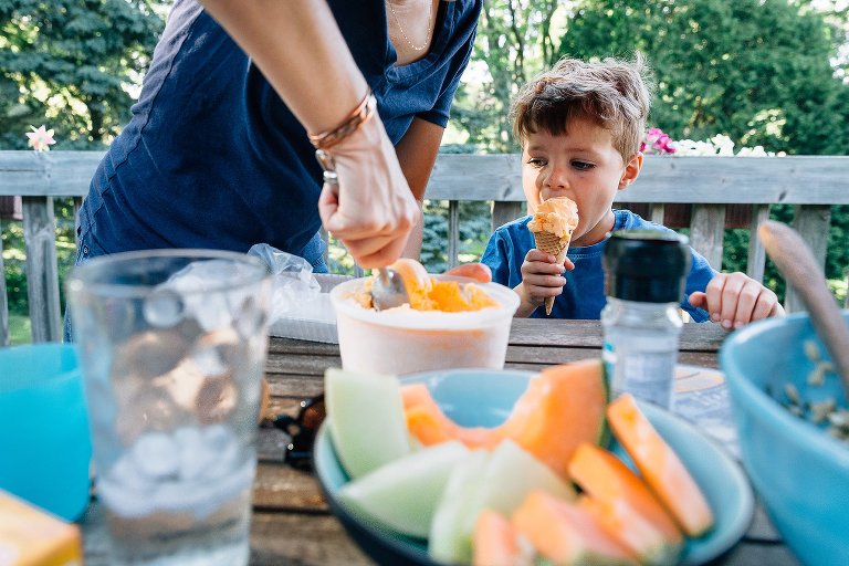 Mother scoops orange sherbet for son. Orange cantaloup in the foreground.
