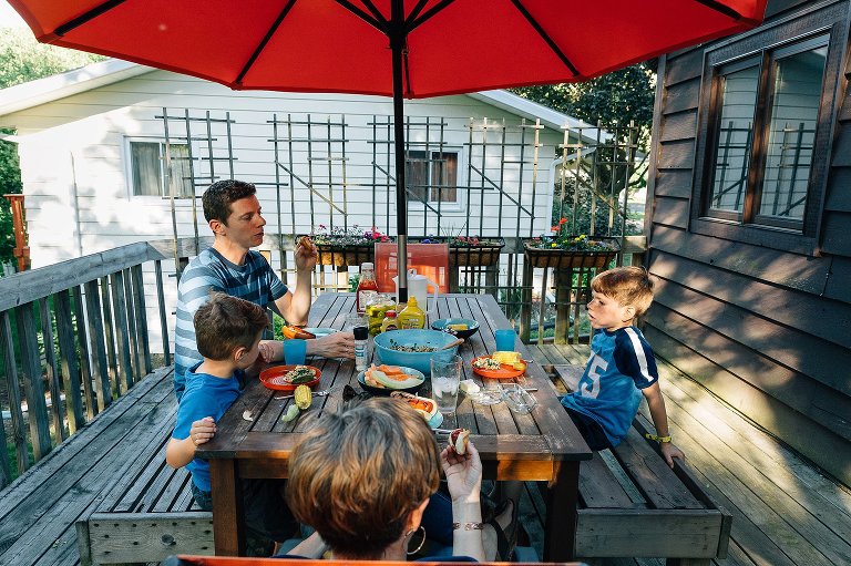 Family of four on deck with picnic table dinner. Sunlight is dappled and family is eating dinner.
