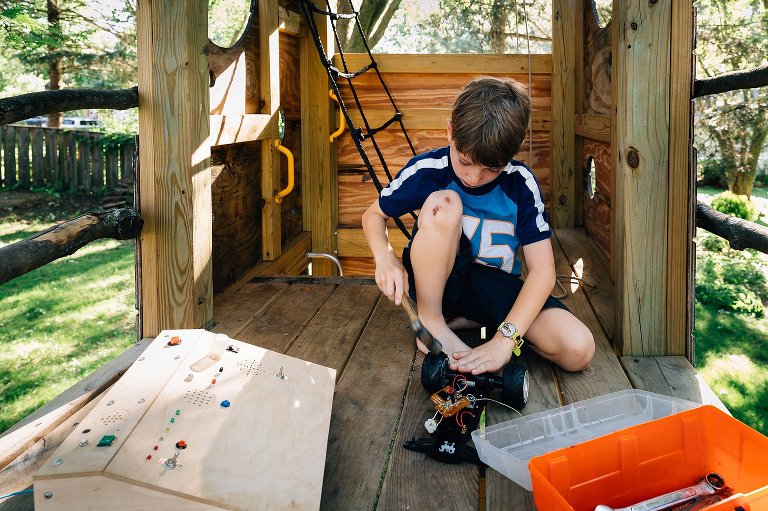 Young boy sits in tree house and works on electrical inventions with toolbox and materials