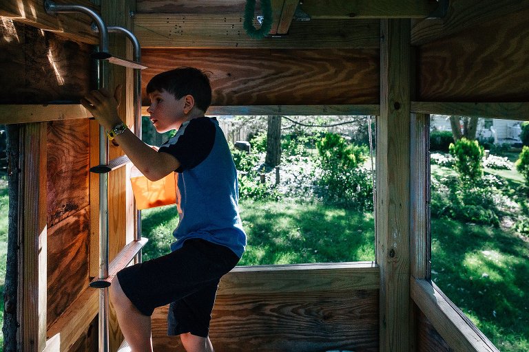 Boy climbs up ladder in backyard treehouse
