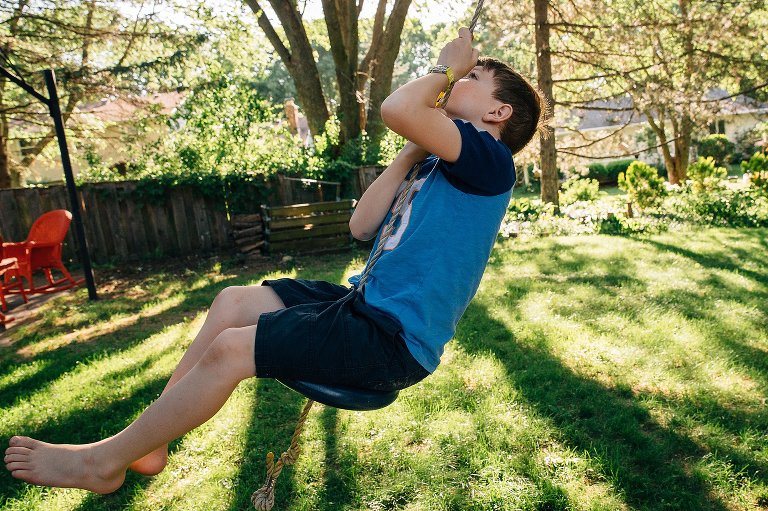 Boy swings on backyard rope in evening summer light