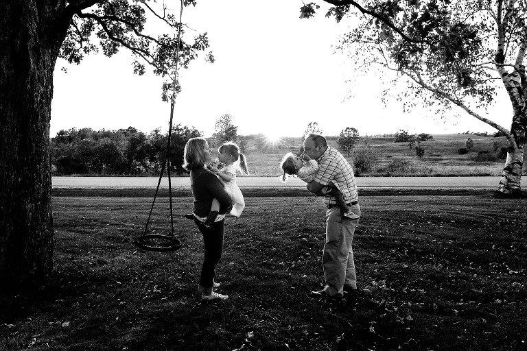 Black and white. Both parents hold their daughters and engage with them at sunset.