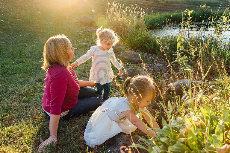 Mom and her two girls explore in the sun next to the pond. 