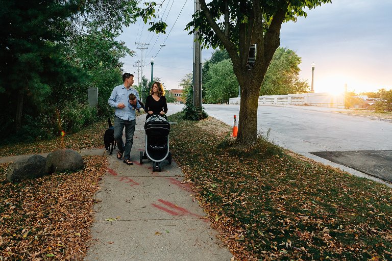 Sun peeks out from behind clouds as parents walk home with dog and infant daughter. 
