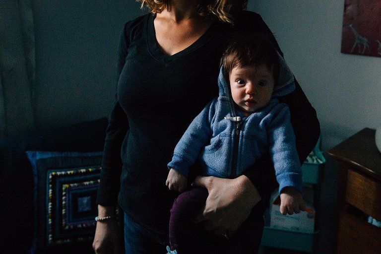 Dramatic low light in bedroom, Mom holds baby. Baby has eye contact with camera. Heavy shadow. 