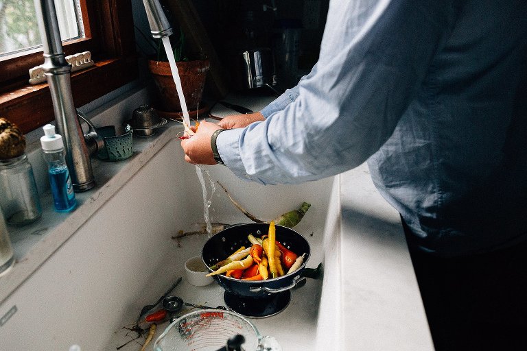 Man washes yellow, orange, and white carrots. 