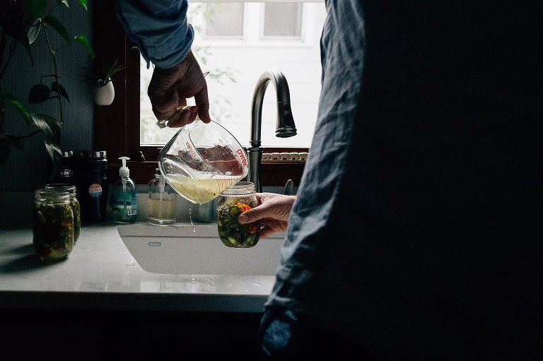 Man adds brine to a jar of pickled jalapenos. 