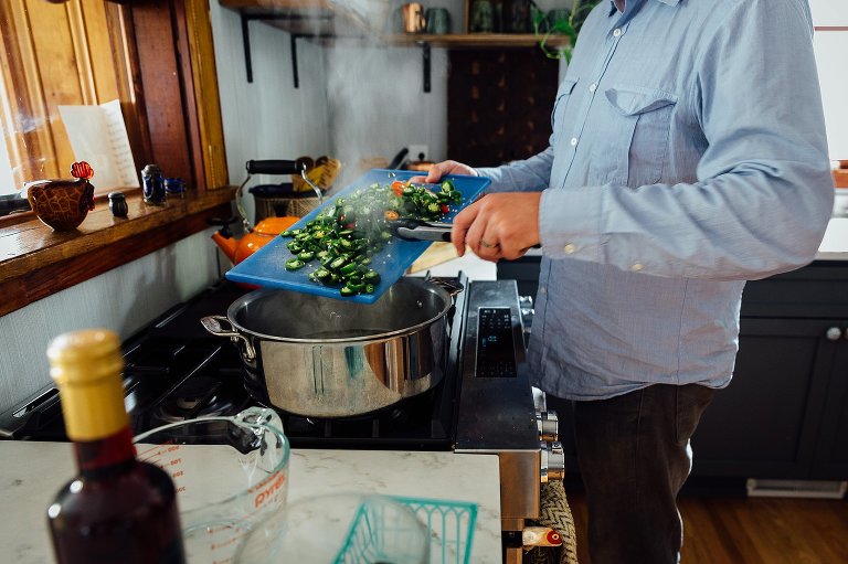 Man adds green and red jalapenos to a steaming pot of water. 