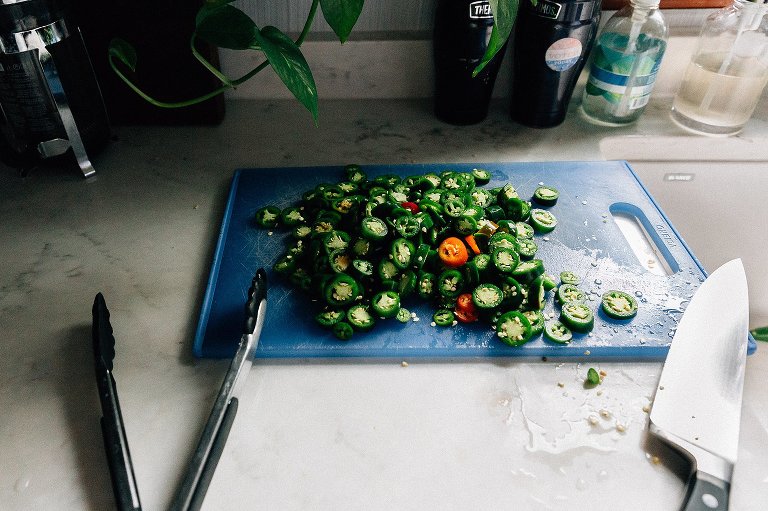 Sliced green and red jalapenos on blue cutting board, white counter top and window light. 