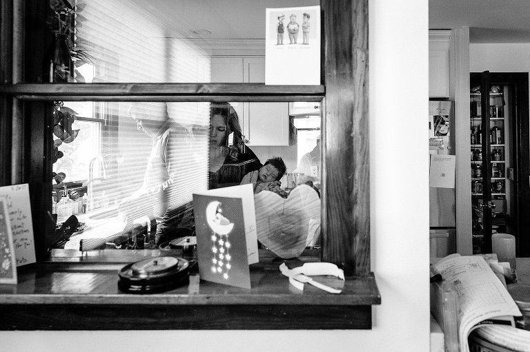 Black and white. Dad and Mom in kitchen. Mom is holding sleeping baby. 
