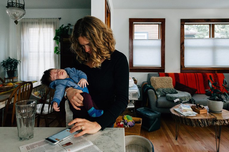 Mom holds sleeping baby while checking phone with other hand.